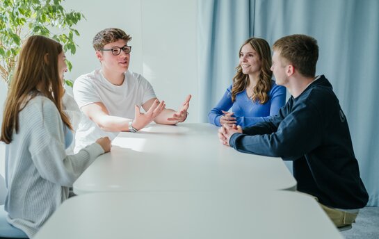 Vier junge Erwachsene sitzen fröhlich an einem Tisch und diskutieren miteinander.