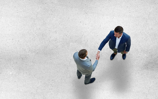 Zwei Männer schütteln sich die Hand, das Bild ist von oben betrachtet. 