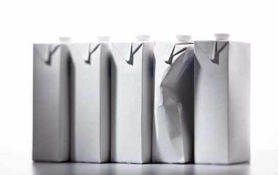 Fünf weiße Getränkekartons stehen in einer Reihe, wobei einer stark eingedellt ist.