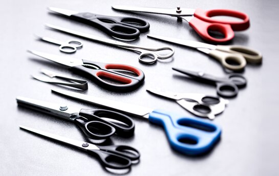 Eine Sammlung verschiedener Scheren mit bunten Griffen liegt auf einem Tisch.
