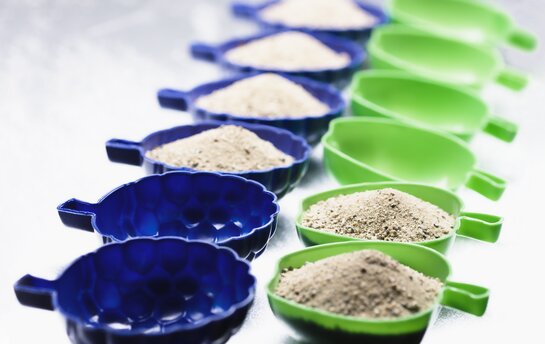 Eine Reihe von blauen und grünen Messbechern, die mit Sand gefüllt sind.