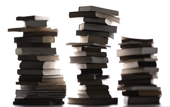 Drei hohe Stapel aus Büchern sind in Silhouette vor weißem Hintergrund zu sehen.