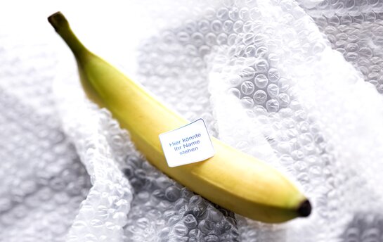 Eine Banane auf Luftpolsterfolie mit einem Etikett, auf dem "Hier könnte Ihr Name stehen" geschrieben steht.