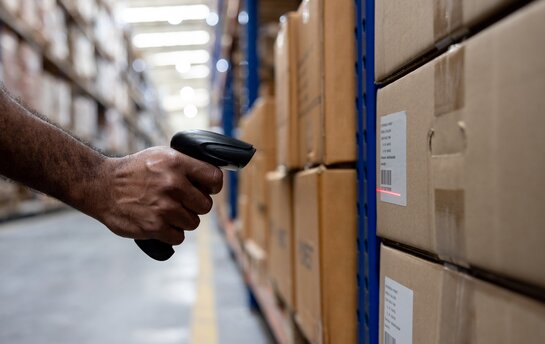 Eine Hand hält einen Scanner, um einen Barcode auf einem Lagerkarton zu lesen.