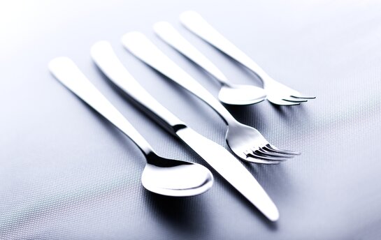 Ein Set aus vier glänzenden Edelstahlbestecken, bestehend aus einem Messer, einer Gabel und zwei Löffeln, liegt elegant auf einem strukturierten Untergrund.