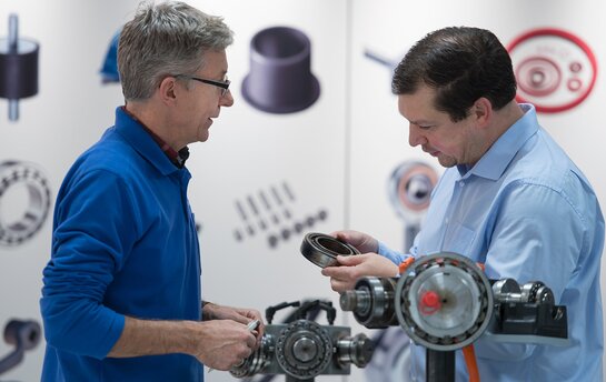 Zwei Männer diskutieren über Maschinenteile in einer technischen Umgebung.