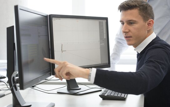Eine Person arbeitet an zwei Computerbildschirmen und zeigt auf den Bildschirm mit einem technischen Diagramm.