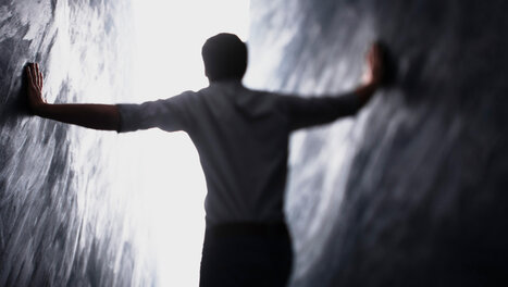 Eine Person steht zwischen zwei hohen Wänden und geht in Richtung eines hellen Lichts.