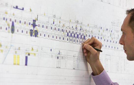 Eine Person zeichnet mit einem Stift auf einem großen technischen Plan.