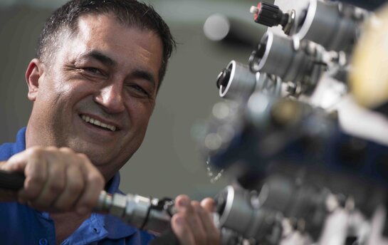 Ein lächelnder Mann in einem blauen Hemd arbeitet an einer technischen Maschine.