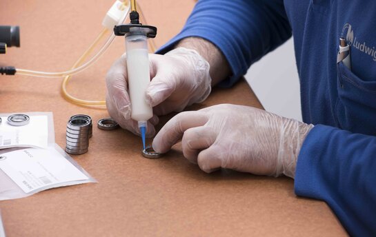 Eine Person in blauen Handschuhen verwendet eine Spritze, um Spezialfett auf kleine Lager aufzutragen.
