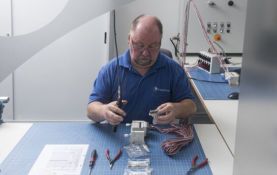 Ein Techniker montiert pneumatische Komponenten an einem Tisch, umgeben von Werkzeugen und Kabeln.
