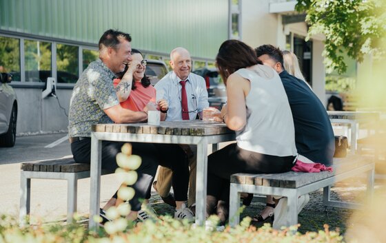 Eine Gruppe von Menschen sitzt im Freien an einem Tisch und unterhält sich fröhlich.